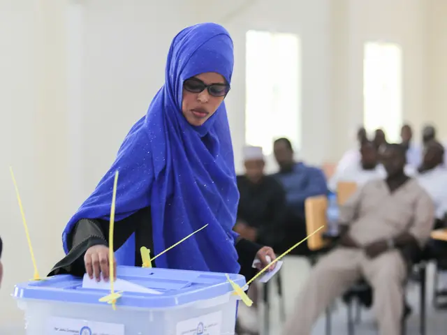 The image shows a woman in a blue headscarf casting her vote at a polling station, surrounded by a...