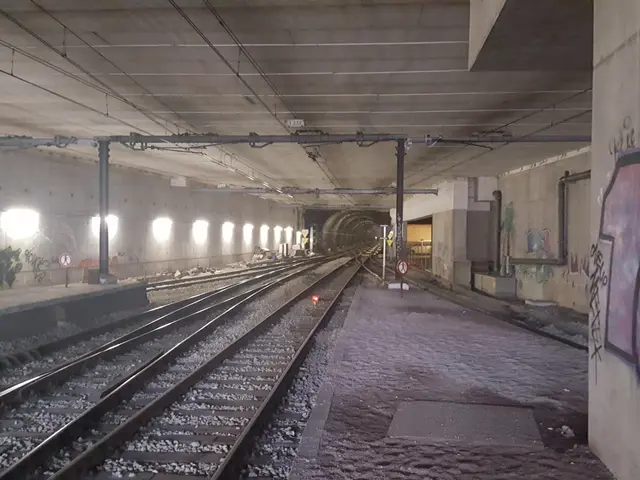 The image shows a train station with a train on the tracks, illuminated by lights on the left side...