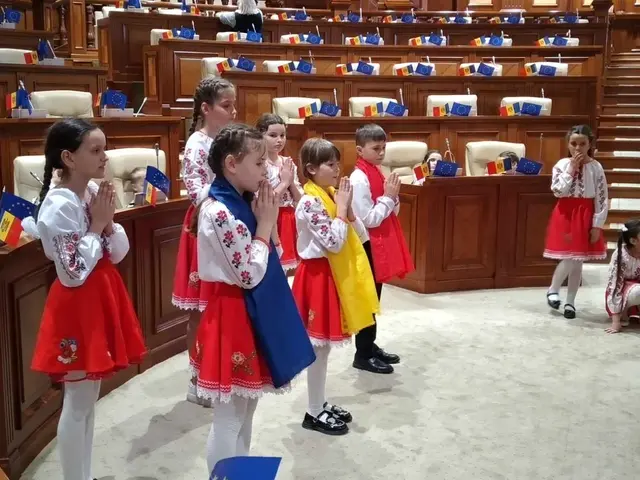 The image shows a group of children standing in front of a large room filled with chairs, tables,...