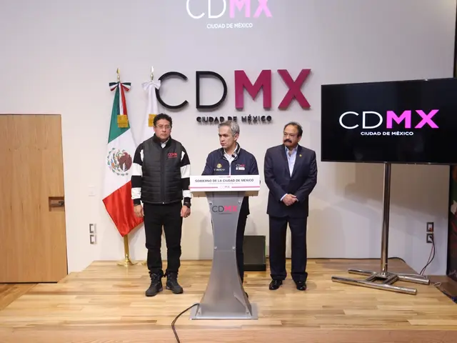 The image shows three men standing at a podium in front of a TV, with a microphone on the podium...