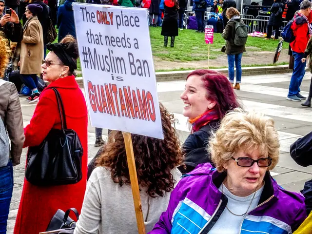 The image shows a group of people standing on the ground, some of them holding bags and one woman...