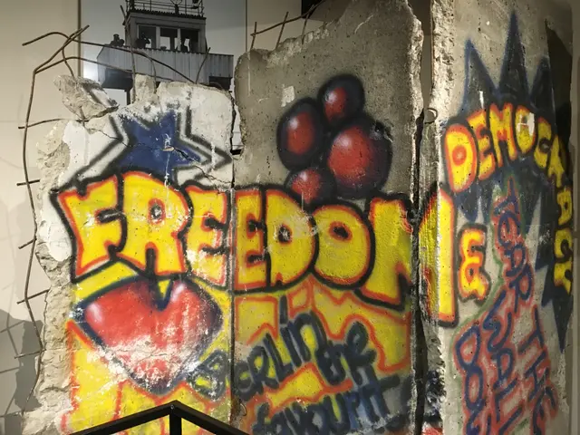 The image shows a wall with graffiti on it in a room, with a railing at the bottom and a building...