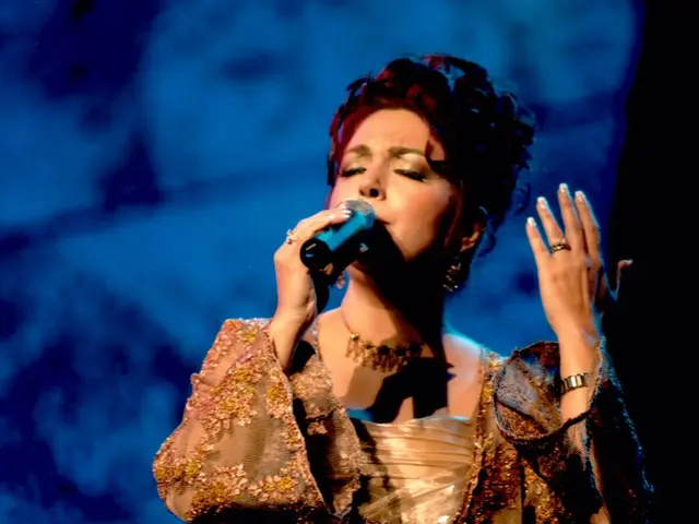 The image shows a woman in a gold dress singing into a microphone, with a blue and black...