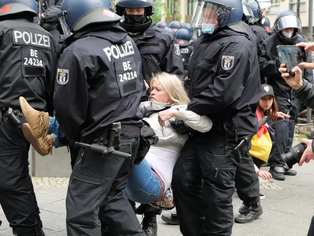 The image shows a group of police officers in riot gear standing around a woman being escorted by...