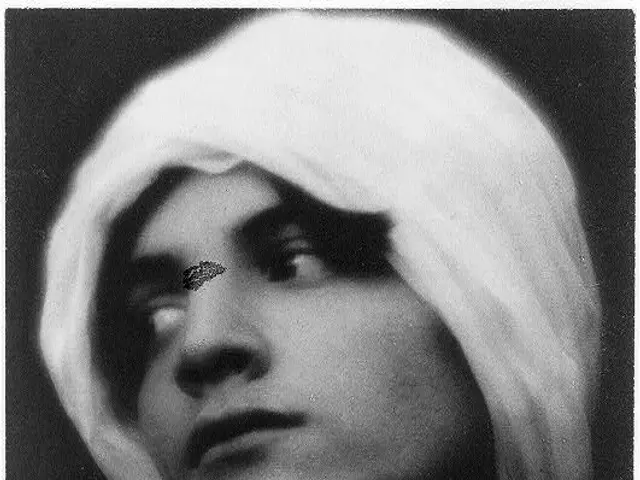 The image shows a black and white photo of a woman with a white turban on her head, set against a...