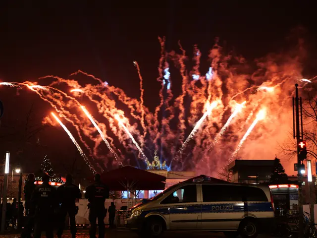 The image shows a police car parked in front of a crowd of people, illuminated by the lights of the...