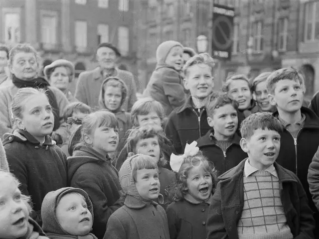 The image shows a group of children standing next to each other in front of a crowd, with a...