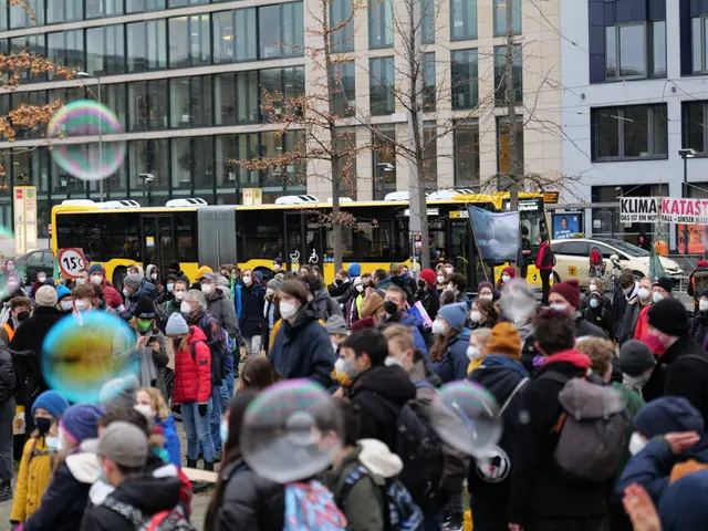 The image shows a large group of people standing in front of a building with windows, trees, and...