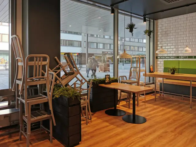 The image shows a restaurant with wooden tables and chairs in front of a large window, surrounded...