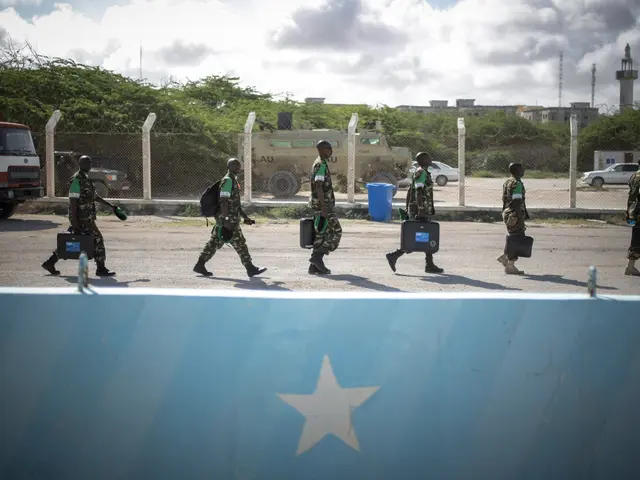 The image shows a group of Somali soldiers walking across a street next to a fence, carrying bags...