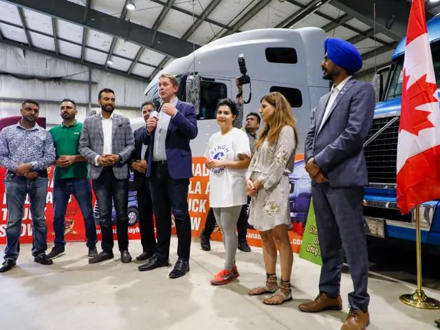 The image shows a group of people standing in front of a truck, with a man holding a microphone and...