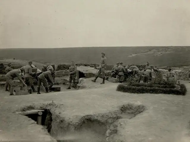 The image shows a group of men standing on top of a dirt field, surrounded by plants and a cloudy...