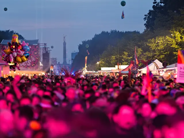 The image shows a large crowd of people at a music festival at night, illuminated by colorful...