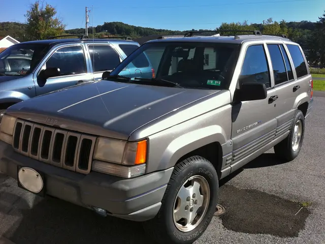 The image shows a silver 1997 Jeep Grand Cherokee parked in a parking lot next to other cars,...