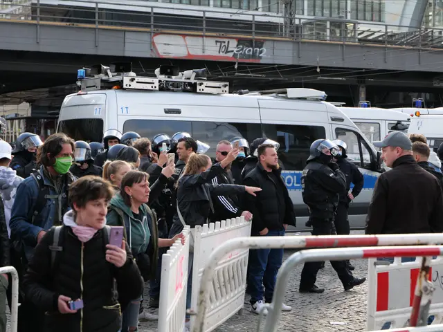 The image shows a group of people standing in front of a line of police vans, some of them wearing...