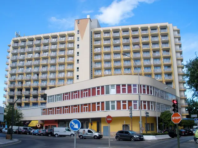 The image shows a large yellow building with many windows on the side of it, surrounded by street...