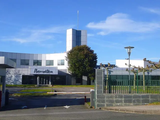The image shows a large building with a lot of windows and a gate in front of it, surrounded by...