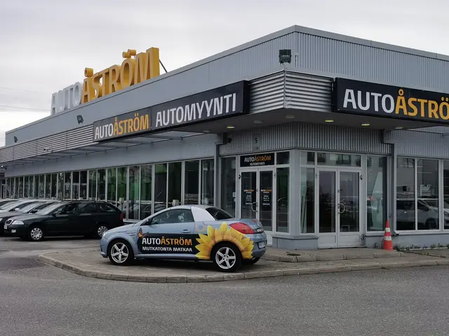 The image shows a car dealership with cars parked in front of it. The building has glass walls and...