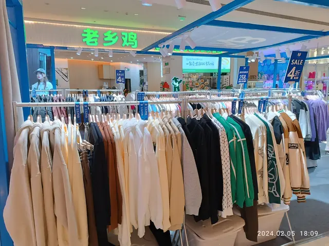 The image shows a clothing store with clothes on display in the middle of it. There are clothes on...