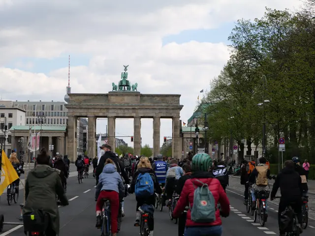 The image shows a group of people riding bicycles down a street in front of the Brandenburg Gate in...