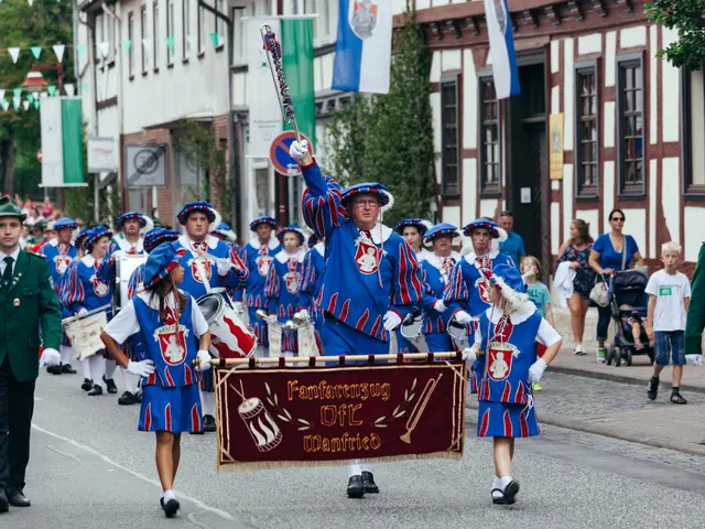 The image shows a group of people walking down a street in a parade, with some of them holding...