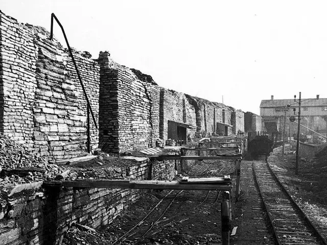 The image shows a black and white photo of a train track with a brick wall on the left side and a...