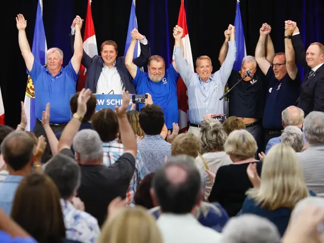 The image shows a group of people standing in front of a crowd of people, some of whom are raising...