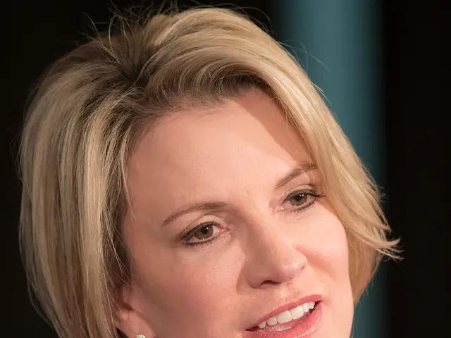 The image shows a woman in a black and white dress with pearls on her neck, speaking into a...