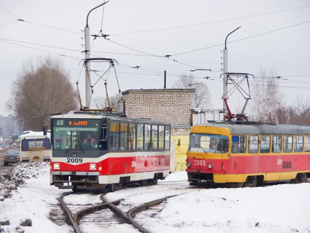 The image shows two red and yellow trams traveling down train tracks in the snow, surrounded by...