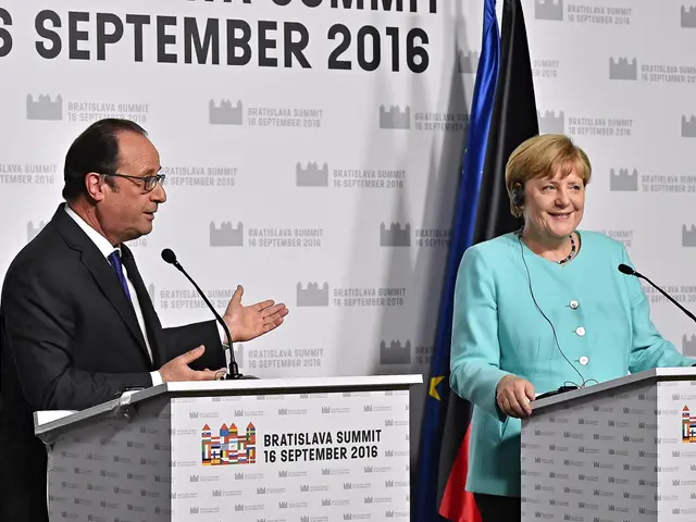 The image shows German Chancellor Angela Merkel and French President Francois Hollande standing in...