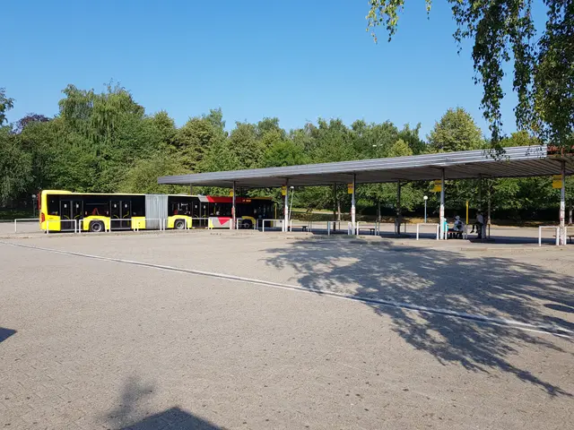 The image shows a yellow bus parked in a parking lot next to a building, surrounded by trees and a...