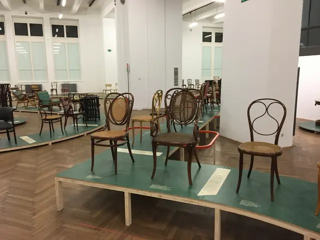 The image shows a room filled with lots of chairs on top of a wooden floor, with a wall in the...