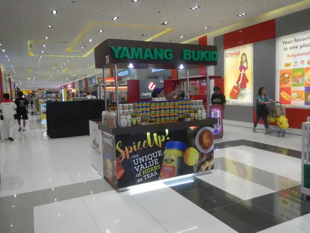 The image shows a bustling shopping mall with people walking around, some of them carrying bags....