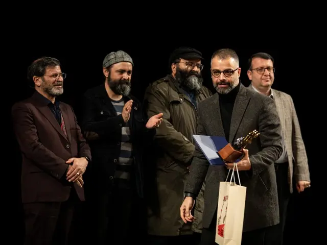 The image shows a group of men standing next to each other on a stage, with one of them holding a...