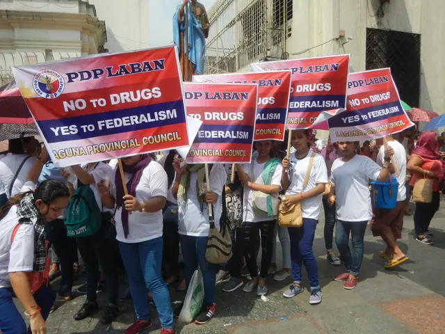 The image shows a group of people walking down a street, holding signs and umbrellas, with a statue...