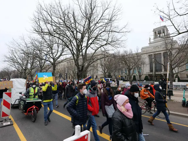 The image shows a large group of people walking down a street in front of a building, some of them...