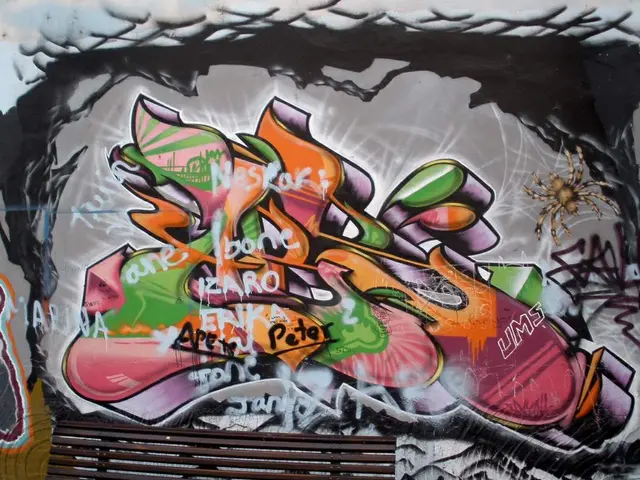 The image shows a wooden bench sitting in front of a wall covered in graffiti. The graffiti is...