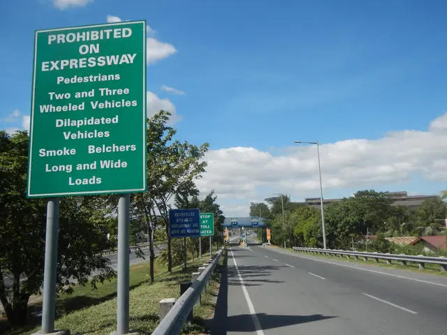 The image shows a highway with a green sign on the side of it that reads "Prohibited on...