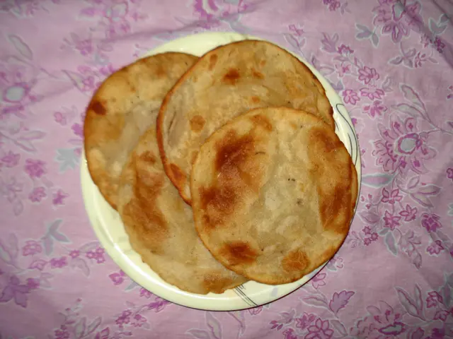 The image shows three flatbreads on a white plate placed on a pink cloth. The flatbread is...