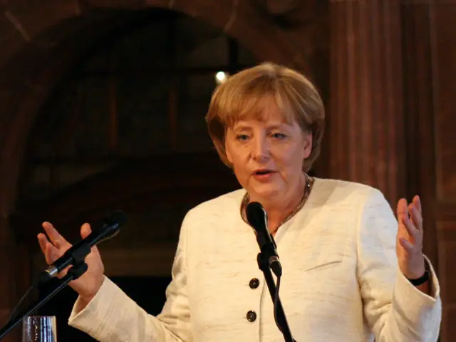 The image shows German Chancellor Angela Merkel delivering a speech at the University of Leipzig....