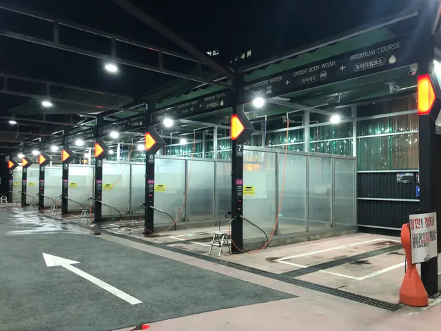 The image shows a parking lot with a lot of cars parked in it, illuminated by lights attached to...