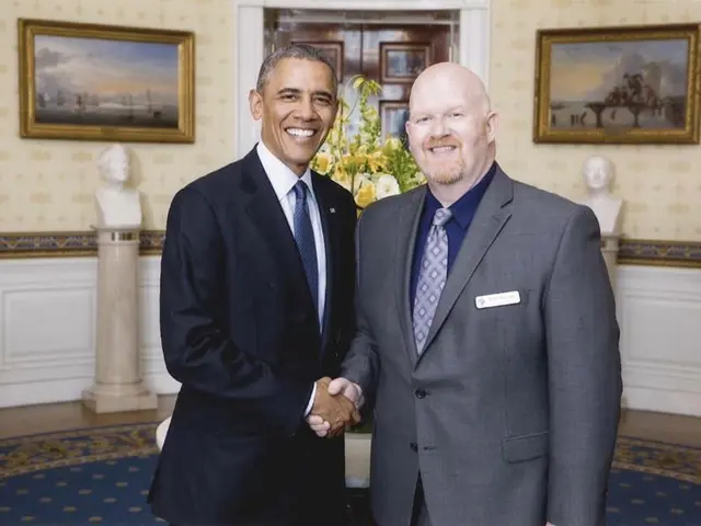 The image shows President Obama and a man in a suit shaking hands in the Oval Room of the White...