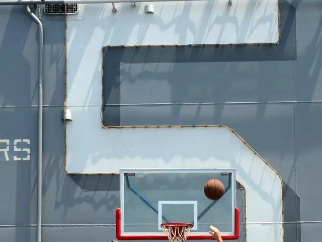 The image shows a group of men playing basketball on a court in front of a large ship. The man in...