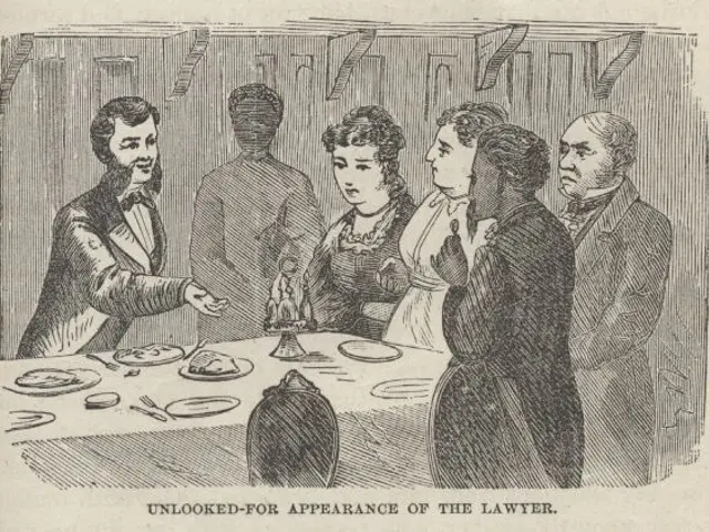 The image shows a group of people standing around a table with plates, spoons, forks, knives, and...