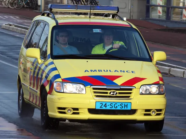 The image shows a yellow ambulance driving down the street with two people inside. On the left side...