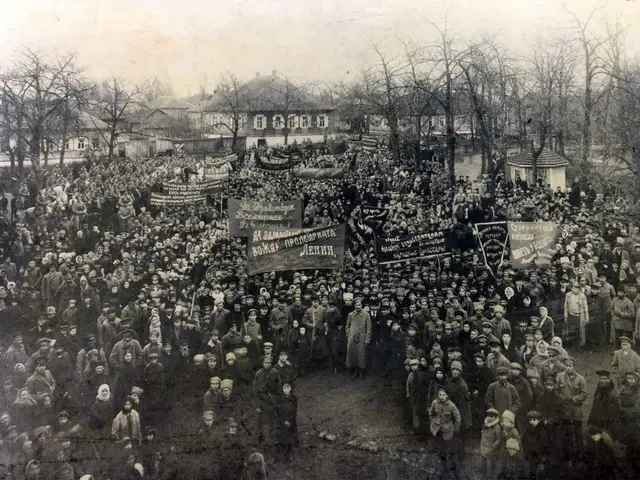 The image shows a large crowd of people standing in front of a building, holding banners with text...