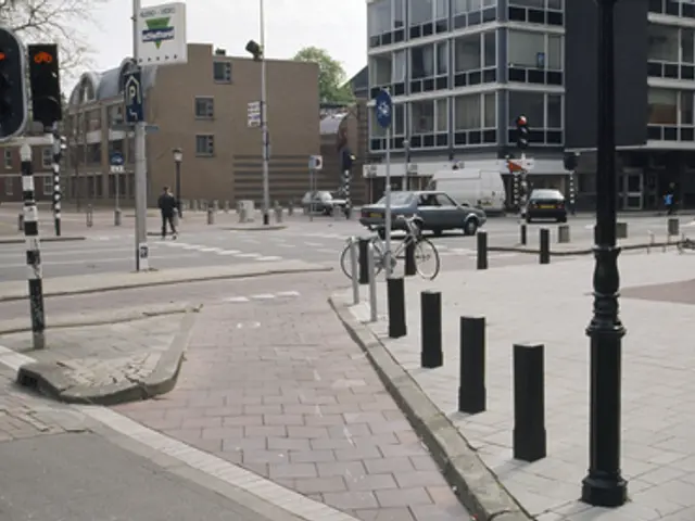 The image shows a city street with a bicycle parked on the side of it. There are vehicles driving...