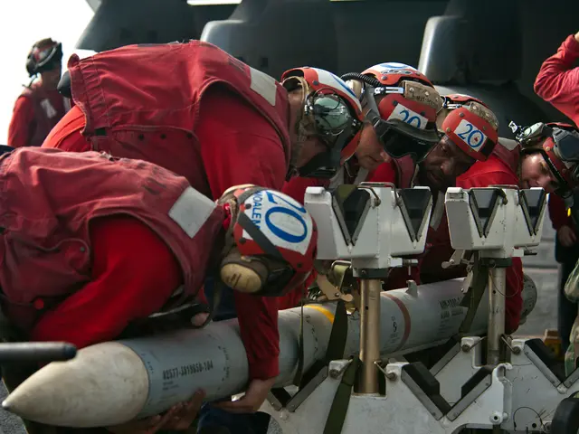 The image shows a group of men in red uniforms and helmets working on a missile, with an aircraft...