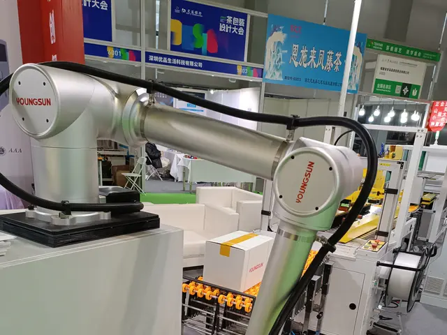 The image shows a robot sitting on top of a table in a room, surrounded by a group of people...