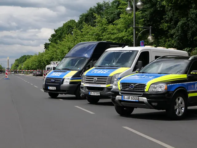 The image shows three police vans parked on the side of a road, surrounded by trees, light poles,...